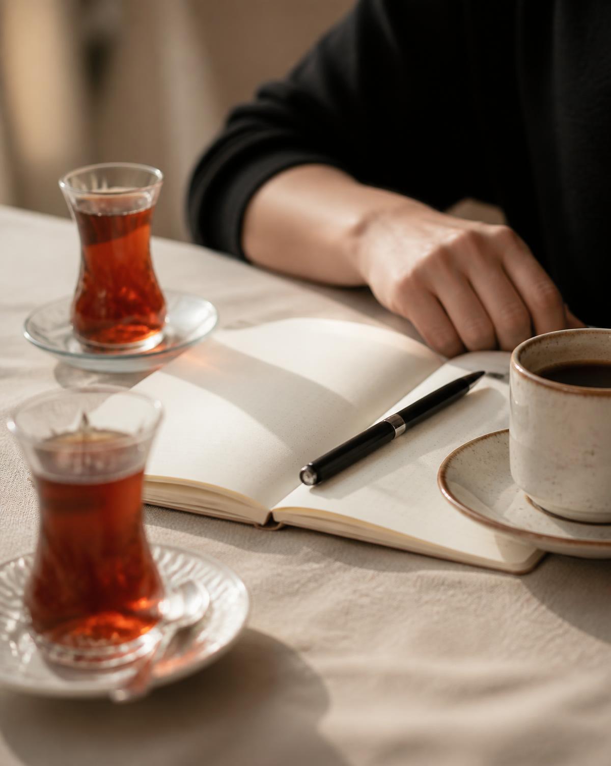 Masada açık defter, kalem, çay ve kahve; toplantı detayı (temsilî görsel)